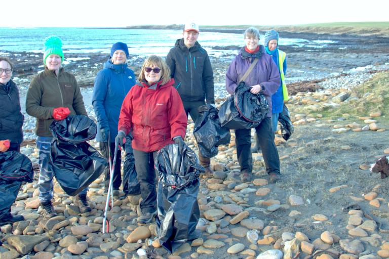A group of volunteers, holding litter picking equipment, are pictured on a beach in Orkney